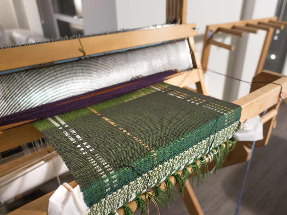 green fabric being woven on a loom