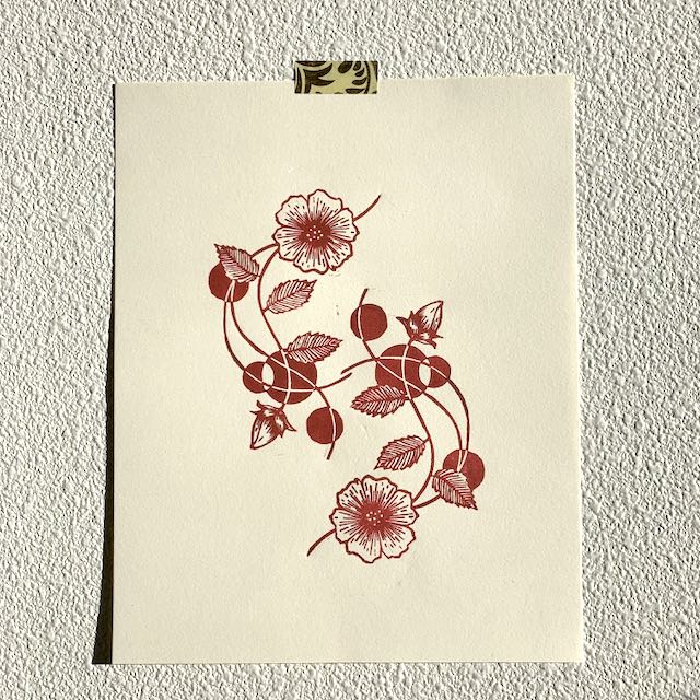 A sheet of cream paper taped to a wall, depicting two entwined floral graphics in dark red ink.