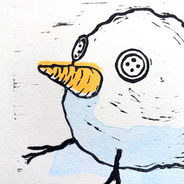 Closeup view of the snowball-bird print. The carrot nose is inked in orange and the shadow along the bottom of the snowball is light blue. Both are slightly mis-aligned from the black outlines of the print.