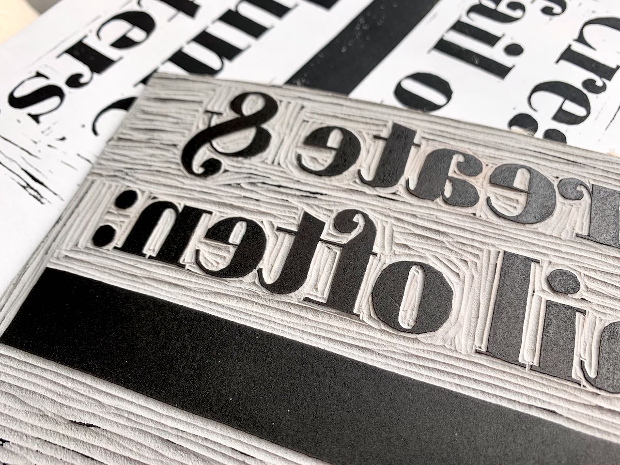 View of a carved grey linoleum block of bold serif letters.