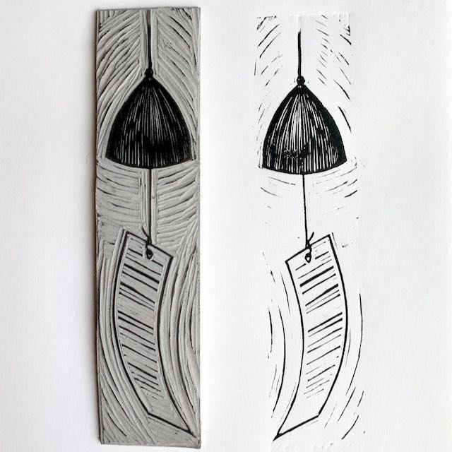 A tall thin carved linoleum block on the left, depicting a Japanese wind chime or furin. On the right is the print created from that block.