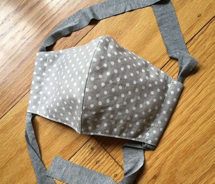 A fitted grey and white polkadot fabric mask. Fabric ties loop through channels at the side of the mask.