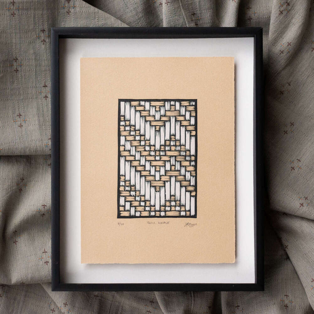 A rectangular print depicting a geometric diagonal twill pattern. The print is on brown paper and is float framed above a white mat within a black metal frame.