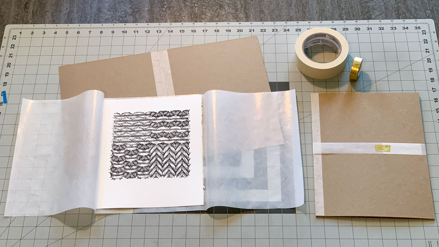 Packing materials laid out across a table. On the left is an open chipboard folder, on top of which is placed a tri-fold sheet of semi-transparent glassine paper folded around a sheep print. To the right is a closed chipboard folder fastened with a glassine belly band.