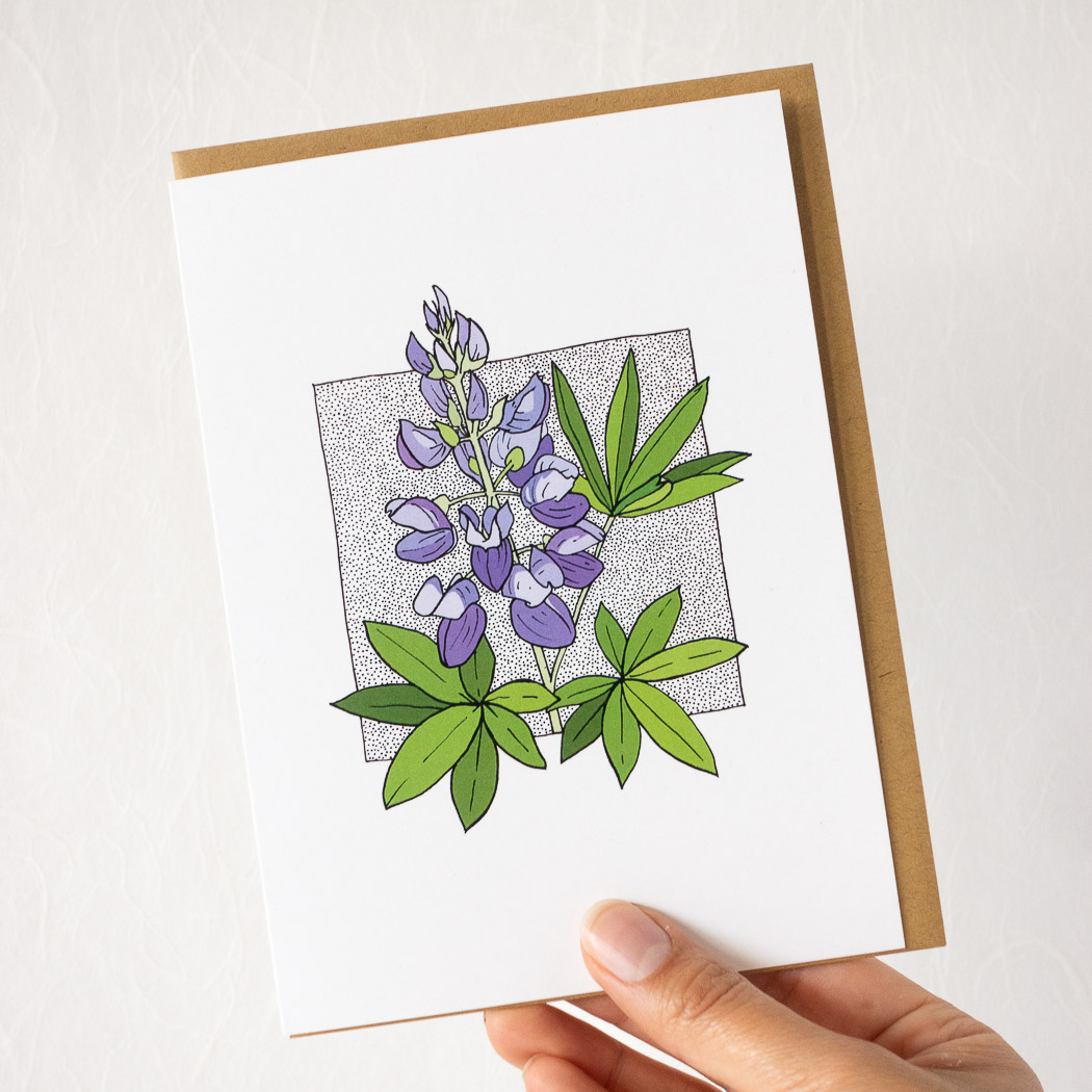 hand holding a white card with a lupine flower, with a brown envelope