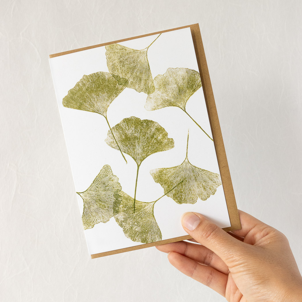 hand holding a white card with ginkgo leaves, with a brown envelope