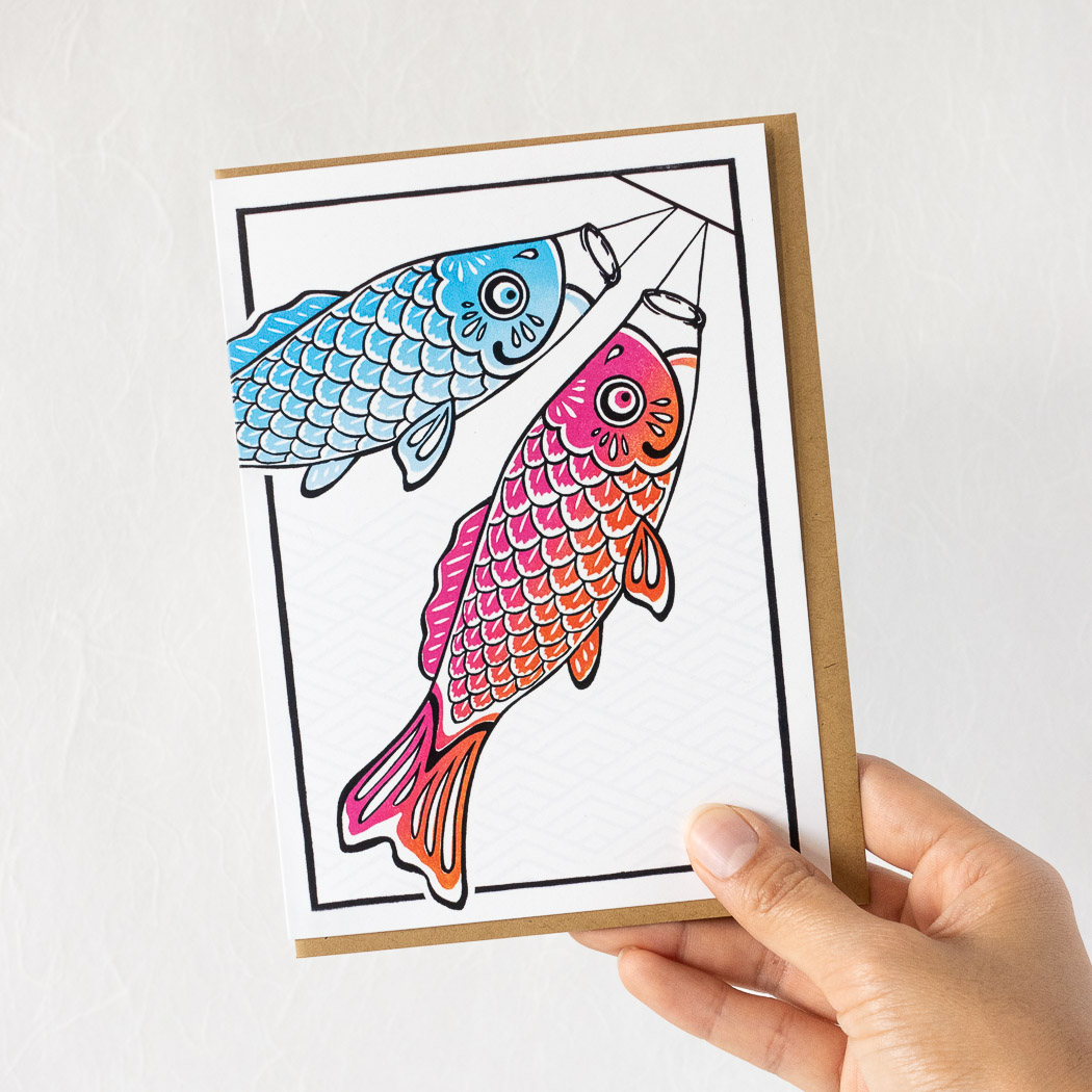 hand holding a white card with two koinobori, with a brown envelope