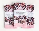 Three rectangular folded kitchen towels, all with the same pink cherry blossom pattern and white packaging band