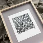 The print lying on grey matboard inside a pale wood frame.