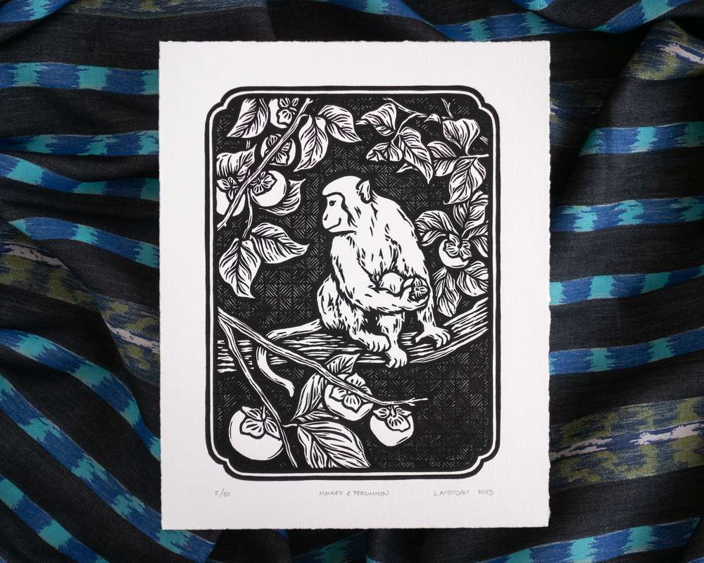 Black and white illustration of a monkey sitting in a persimmon tree. The white paper sits on top of rumpled blue striped fabric.
