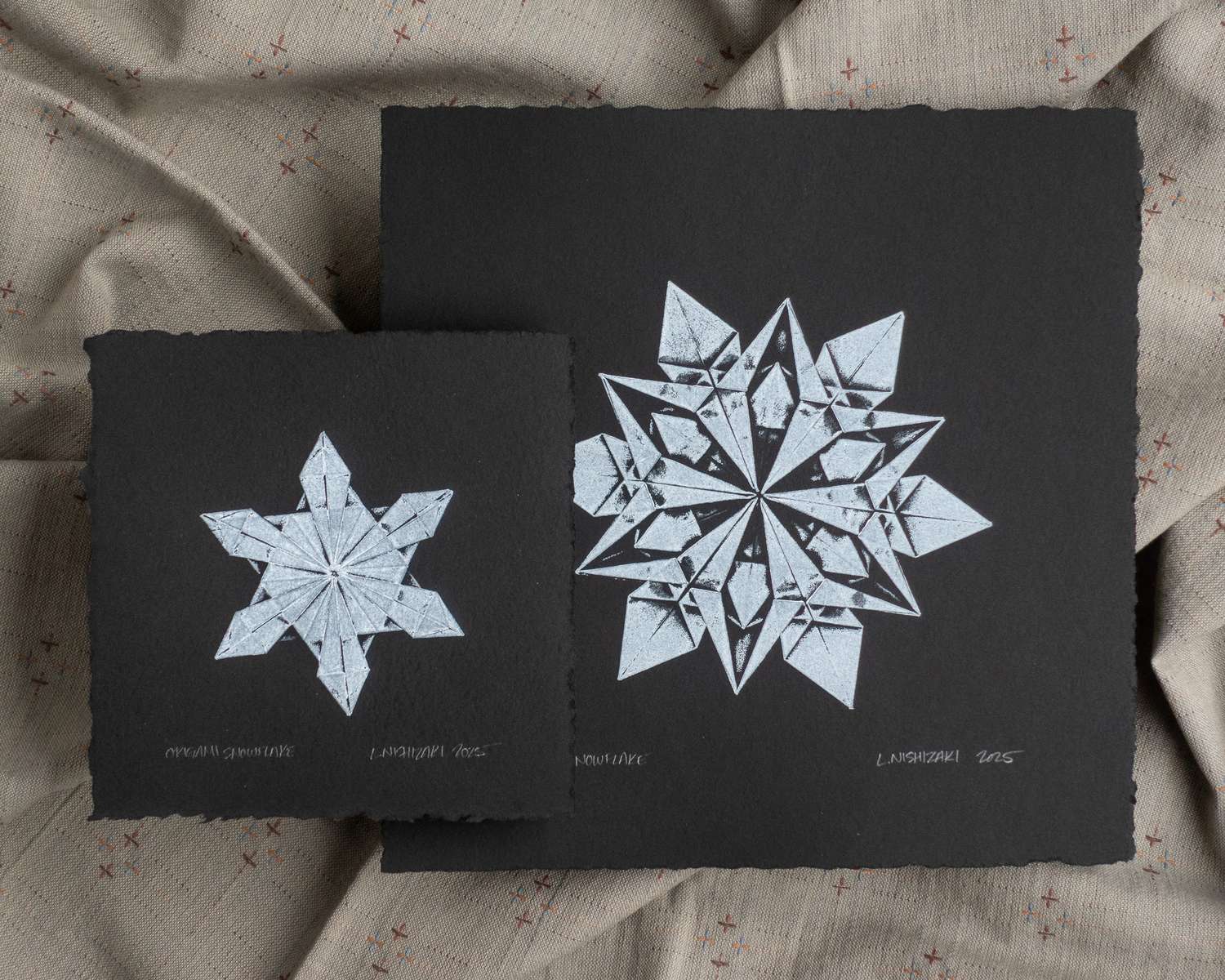 Two black and white monoprints of origami snowflakes; white impressions on square black paper.