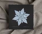 A white impression of an origami snowflake on square black paper.