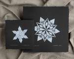 Two black and white monoprints of origami snowflakes; white impressions on square black paper.