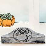 A grey carved linoleum block with black ink on the raised sections. The colored persimmon print is behind the block.