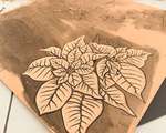 A brown linoleum block with a partial carving of two poinsettia flowers.