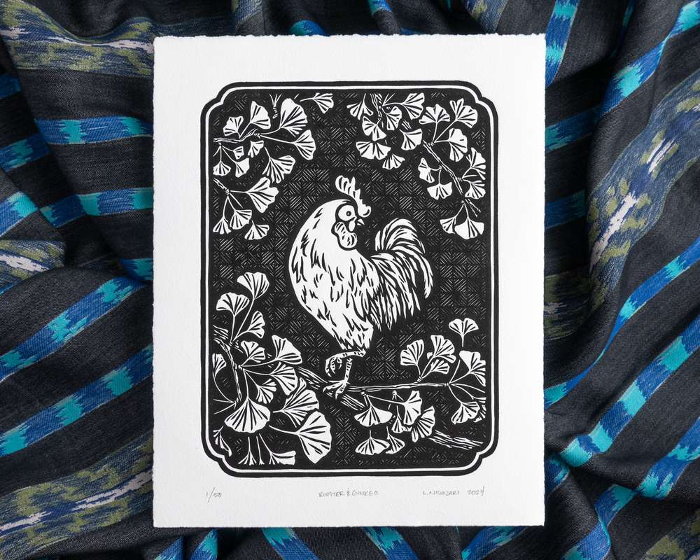 Black and white illustration of a rooster in a ginkgo tree. The white paper sits on top of rumpled blue striped fabric.