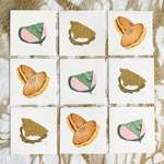 9 square prints arranged in a 3x3 grid on a gold-flecked backdrop. There are 3 print designs depicting kashiwa mochi, dorayaki, and sakura mochi.