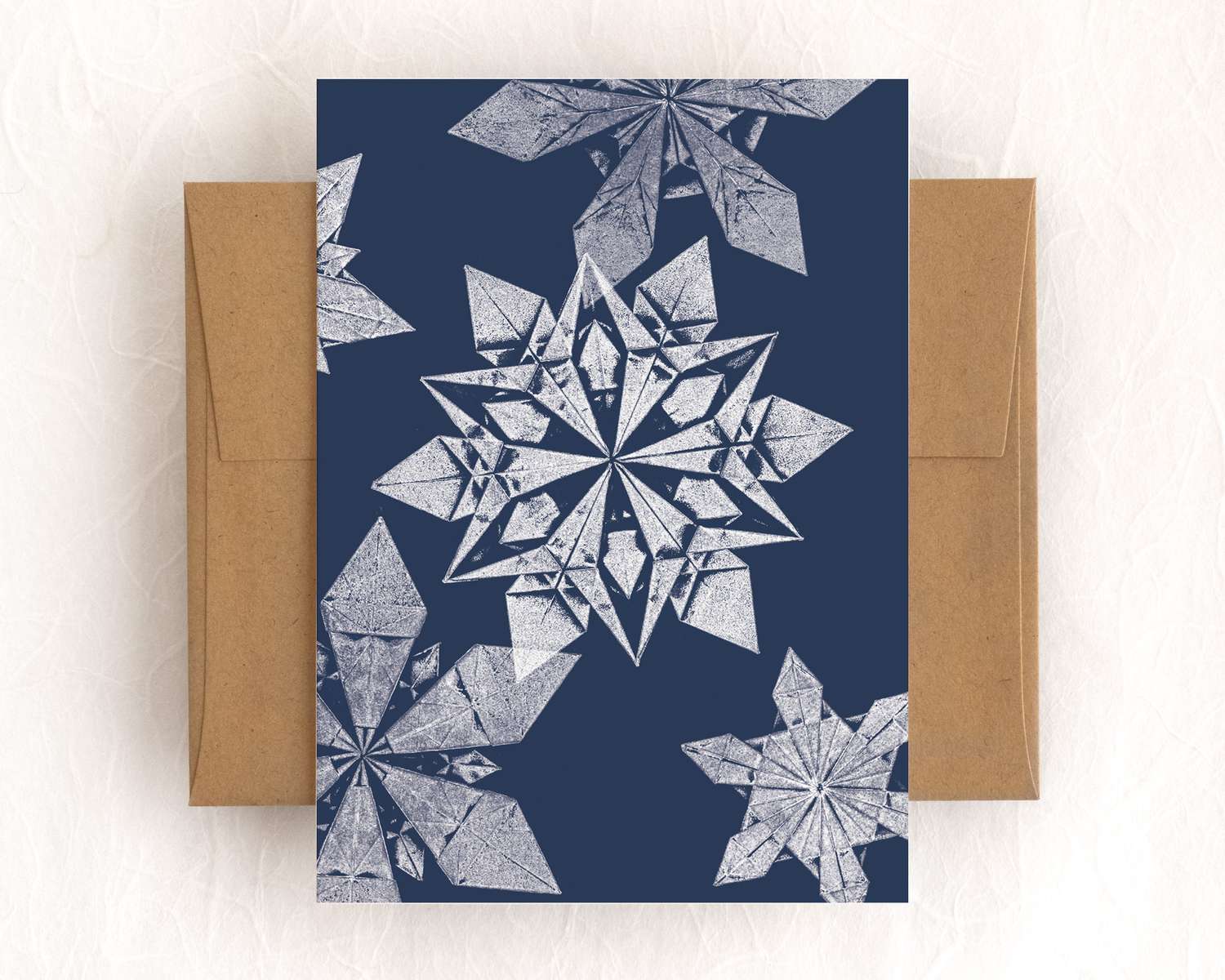 A single card with a brown envelope. The card depicts a five white impressions of origami snowflakes on a navy background.
