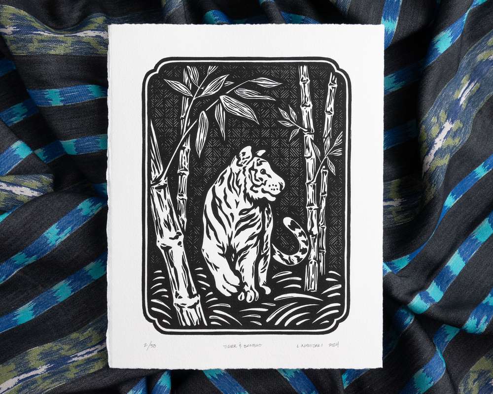 Black and white illustration of a tiger amongst bamboo. The white paper sits on top of rumpled blue striped fabric.