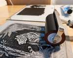 A grey carved linoleum block featuring a tiger, half-inked in black ink. A red brayer covered in black ink rests on top of the block and a glass inking plate with more ink sits in the background.